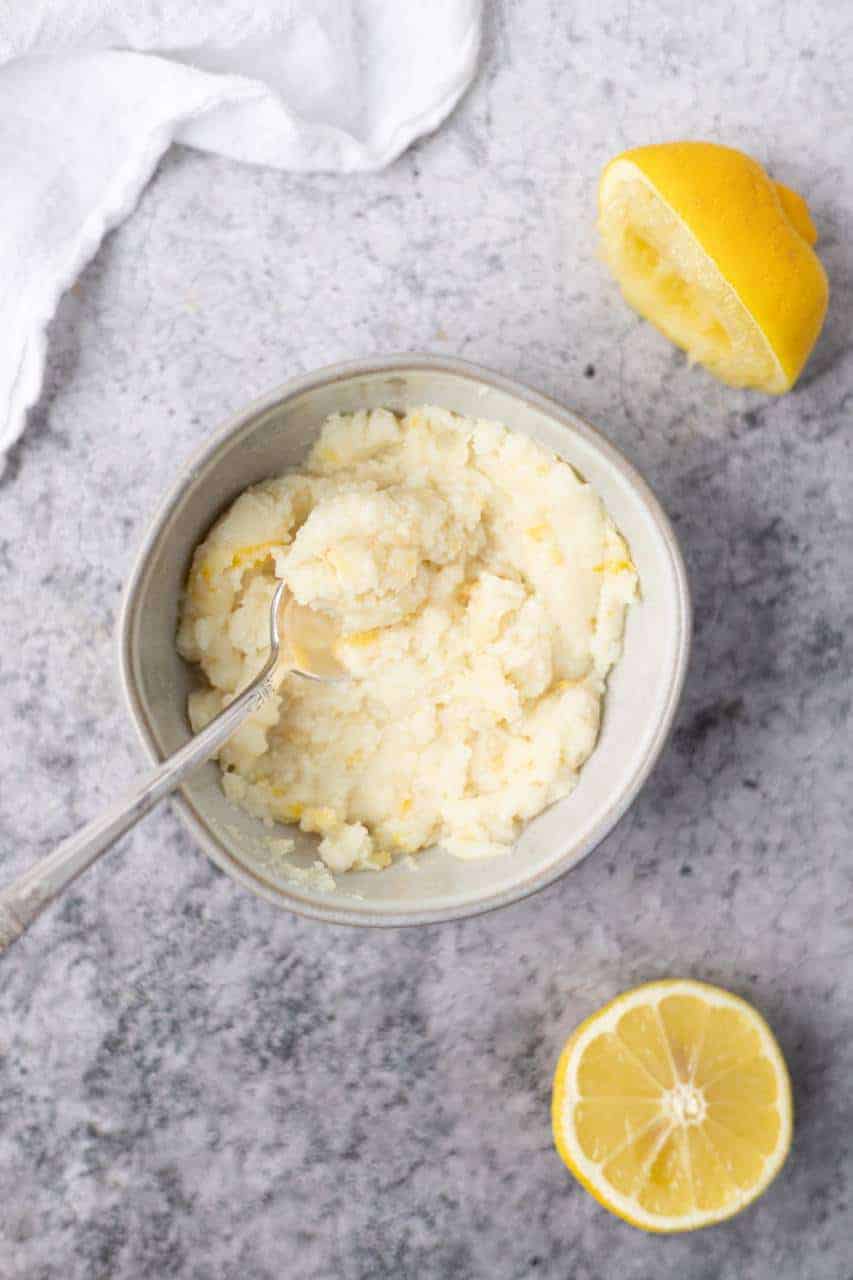 mashed potatoes in a bowl with spoon and a lemon cut in half